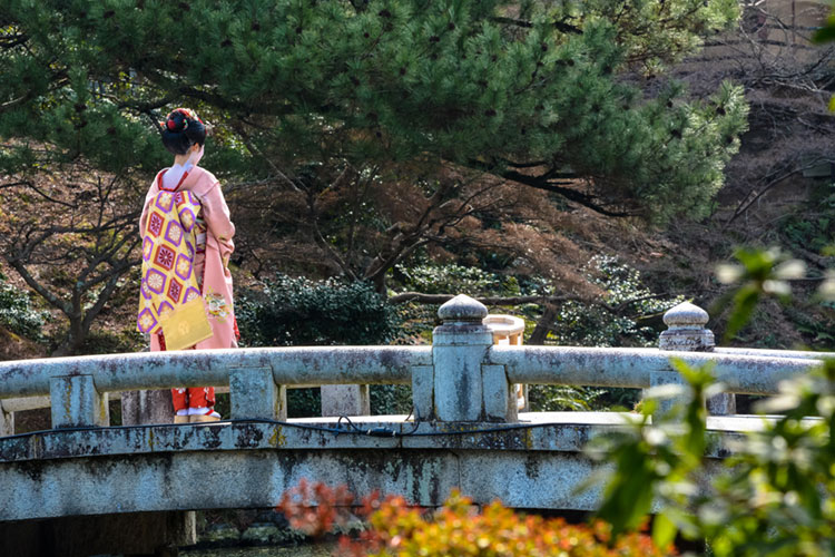 Tourist in maiko outfit standing on a bridge at Maruyama Park in Kyoto.